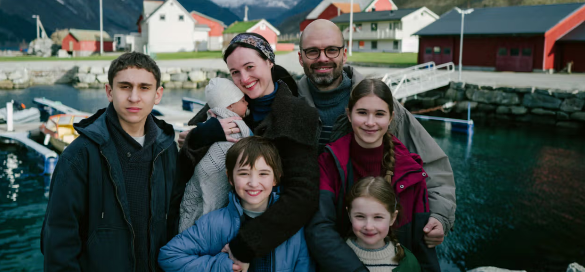 En familie som står på kaia med fjell i bakgrunnen - Klikk for stort bilde
