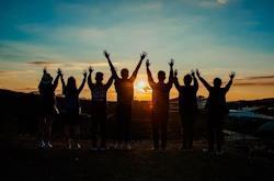 Sju ungdommer strekker armene i været i solnedgang